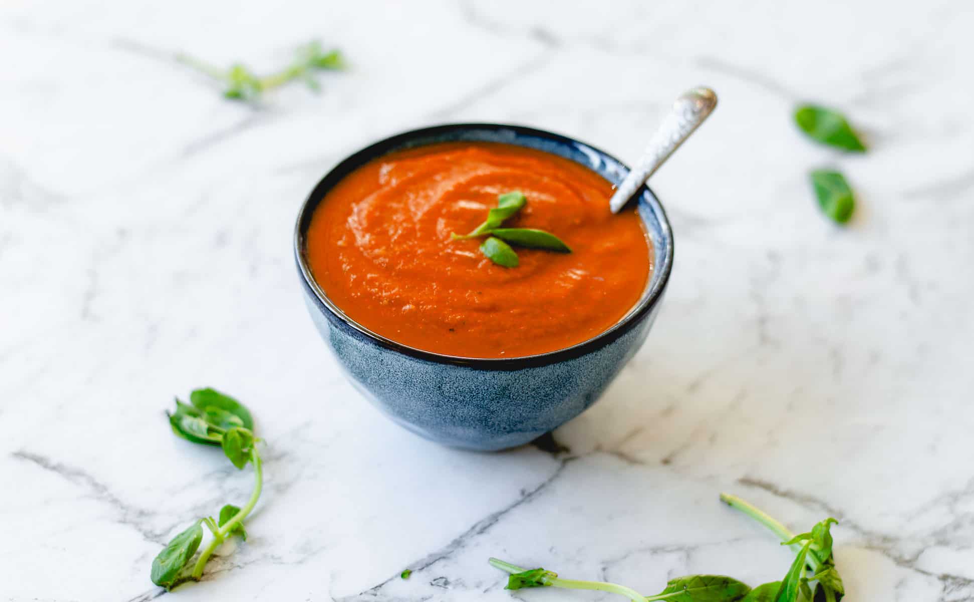 Tomato soup in blue bowl with fresh basil.