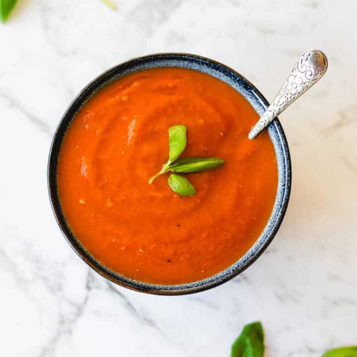 Homemade tomato soup with basil in a blue bowl.