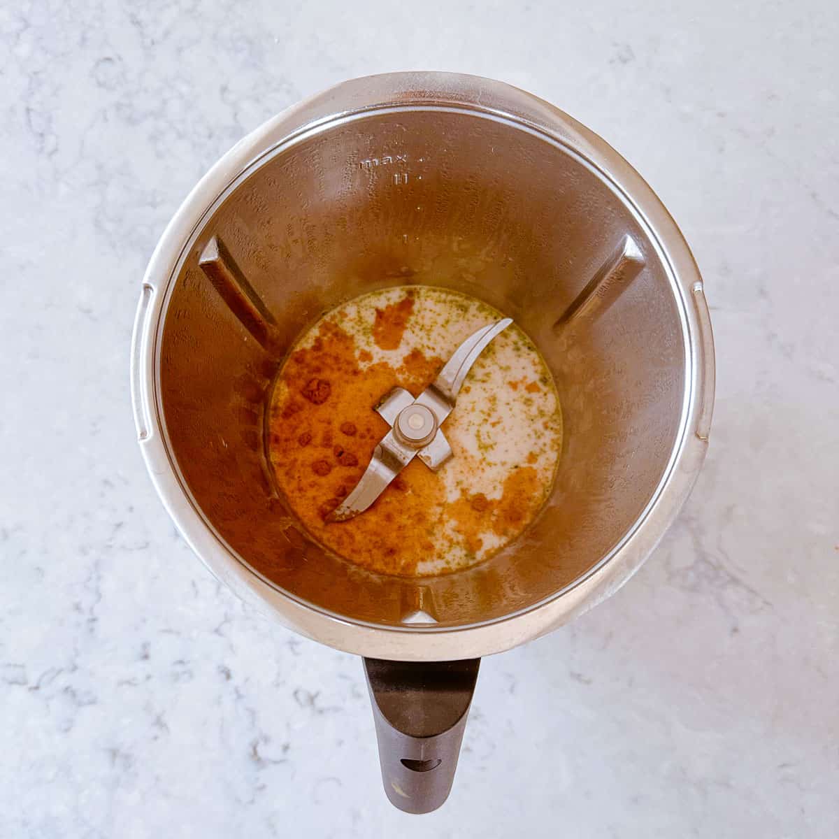 Cinnamon and Matcha powder added to hot milk in a Thermomix jug.