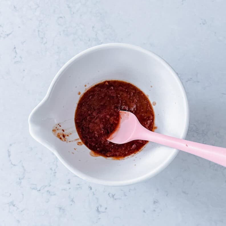 Mashed dates in a cream bowl with pink spatula.