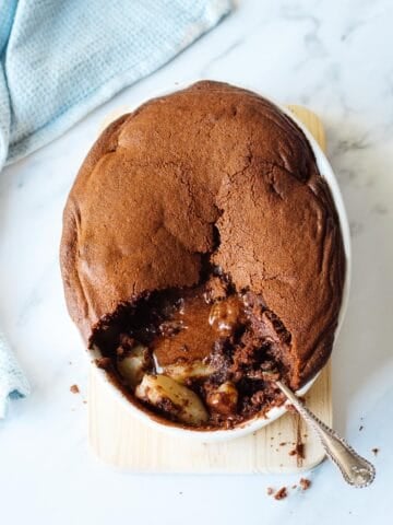 Chocolate Pear Pudding in an oval dish on a marble bench top, with blue tea towel on the side.