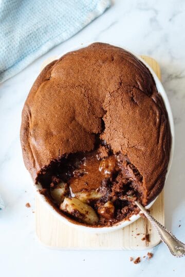Chocolate Pear Pudding in an oval dish on a marble bench top, with blue tea towel on the side.