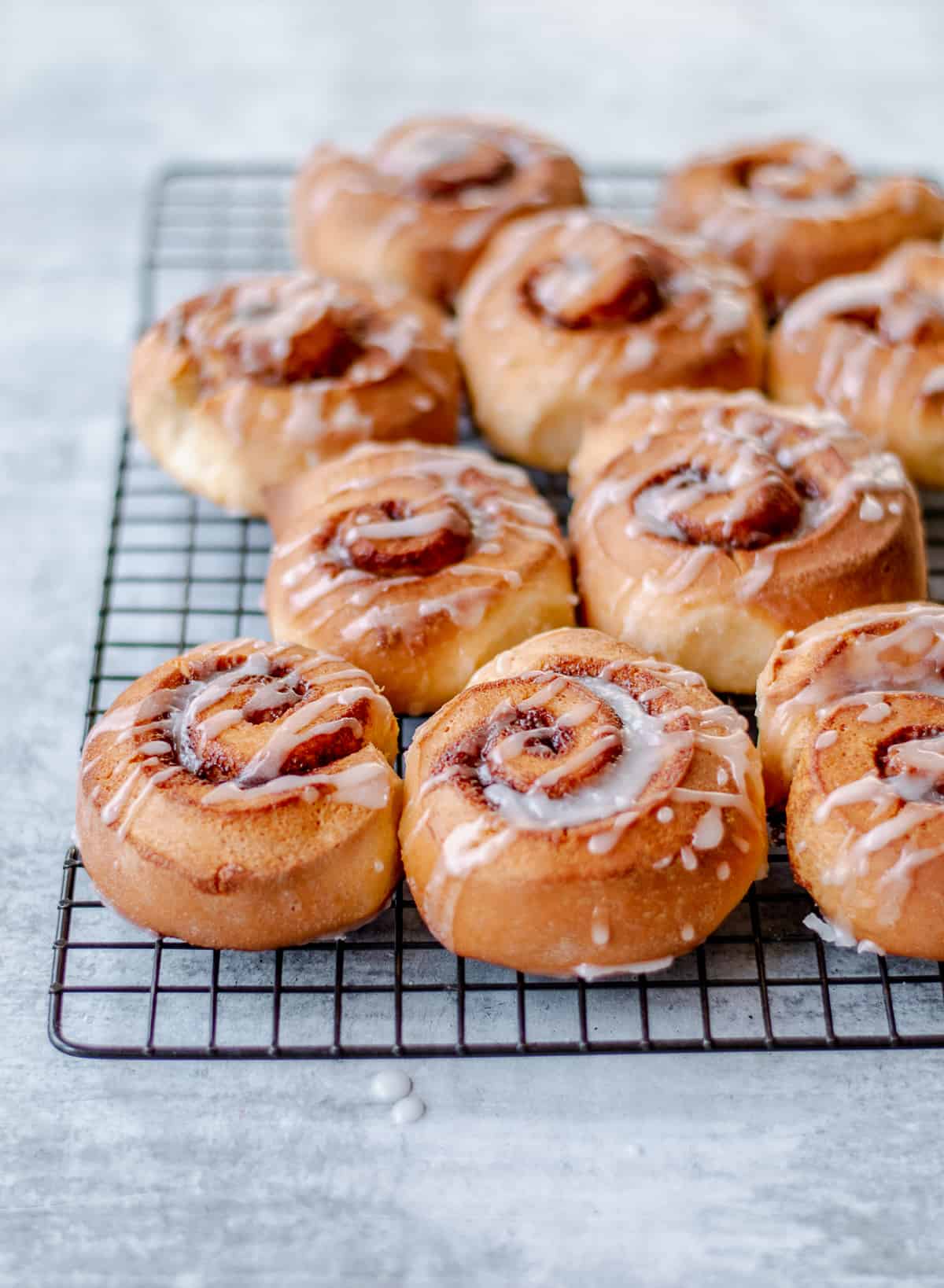 Homemade Cinnamon Rolls on wire baking rack drizzled with white icing