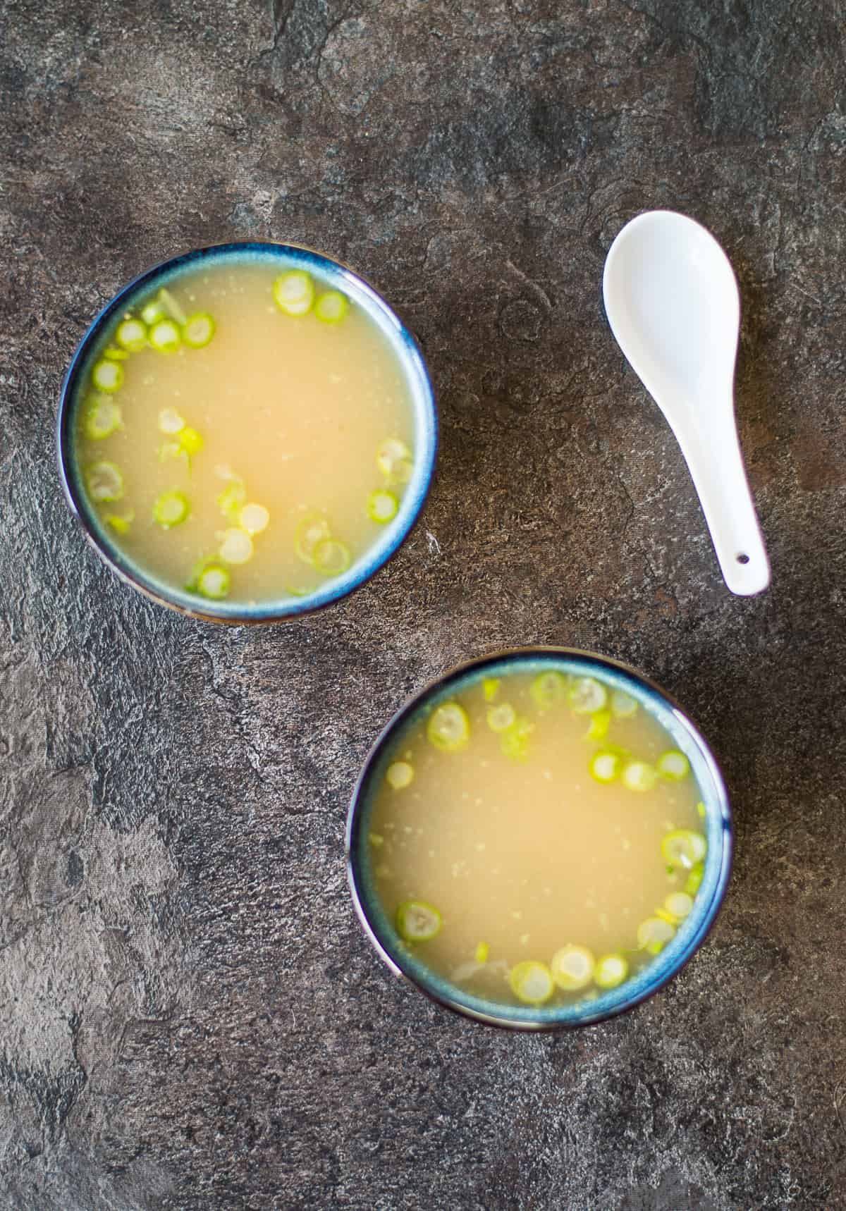 2 bowls of miso soup with spring onions and a white spoon