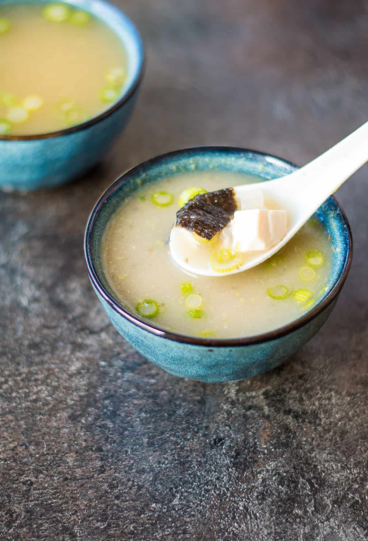 A blue bowl of miso soup with a white spoon