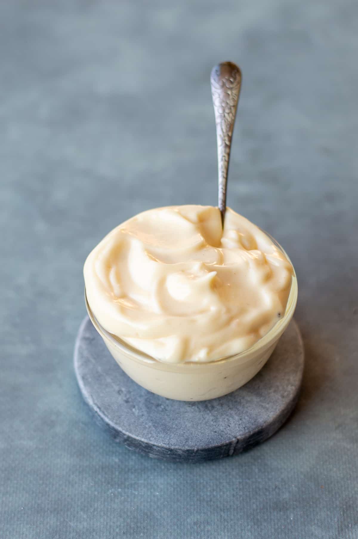 A bowl of homemade egg mayonnaise with a spoon on blue background