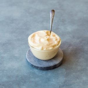 A bowl of homemade Mayonnaise with a silver spoon on blue background