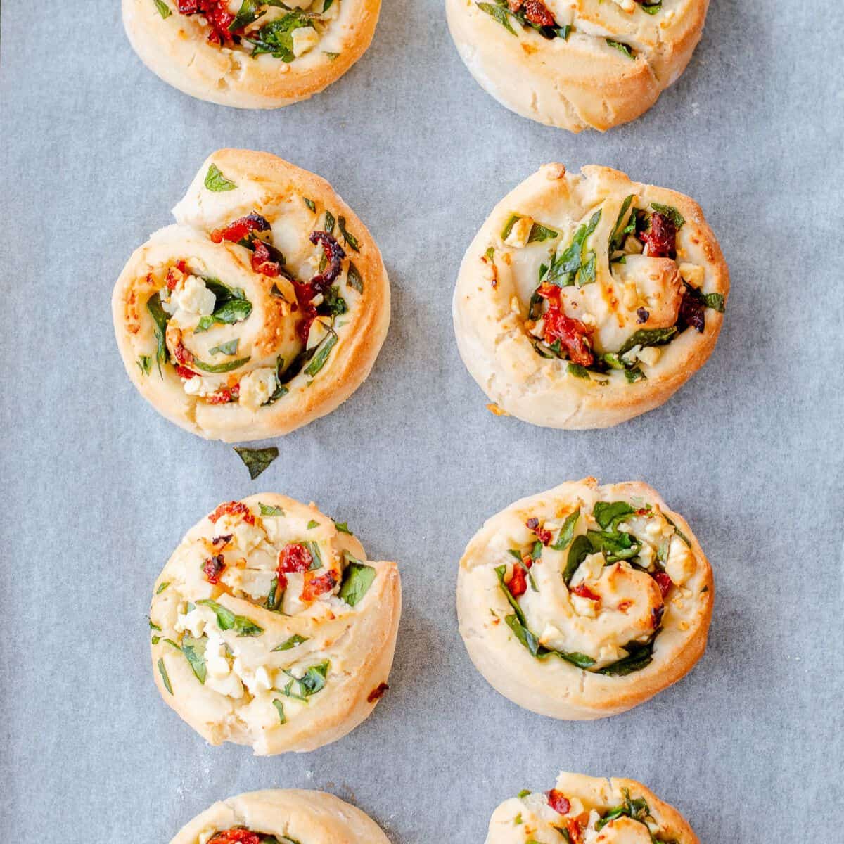 Spinach, feta and sundried tomato scrolls on a baking tray.