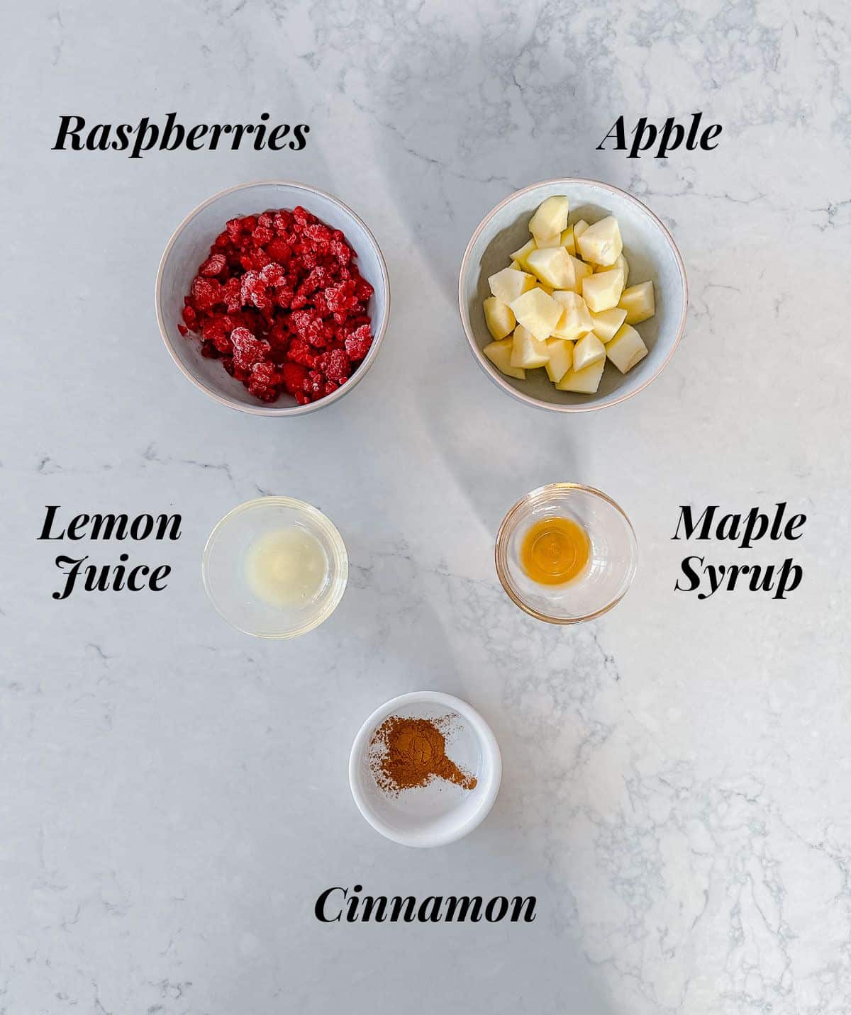 A bowl of raspberries, apples, maple syrup, cinnamon and lemon juice.