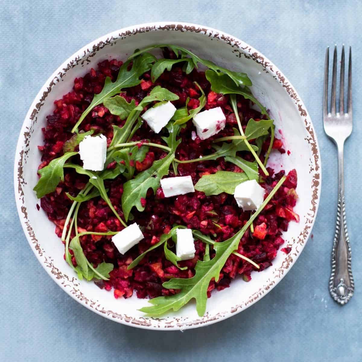 Beetroot, feta and rocket salad in white bowl with fork