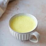 A mug of turmeric latte on a grey background.