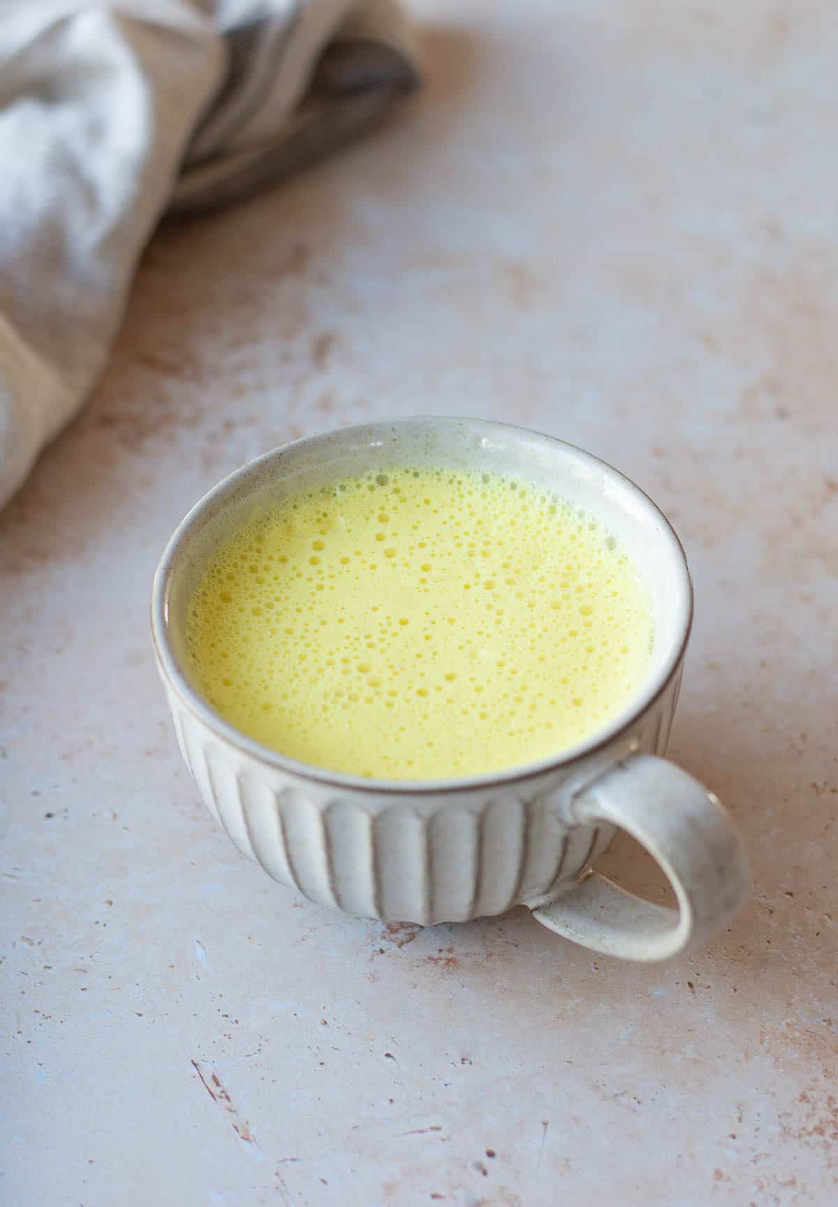 A mug of turmeric latte on a grey background.