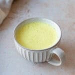 A mug of turmeric latte, sitting on a grey background.