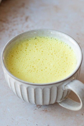 A mug of turmeric latte, sitting on a grey background.