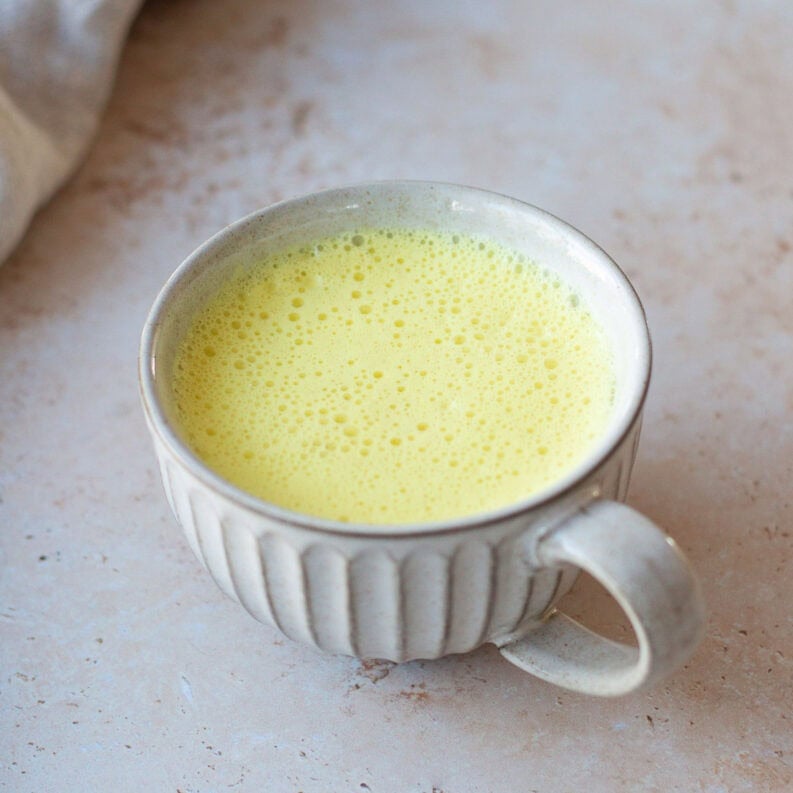 A mug of turmeric latte, sitting on a grey background.