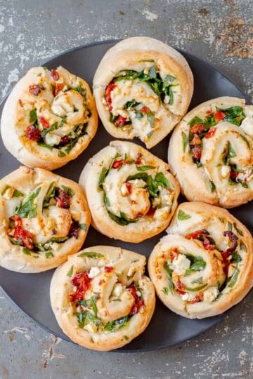 Seven spinach feta sundried tomato scrolls on a dark plate