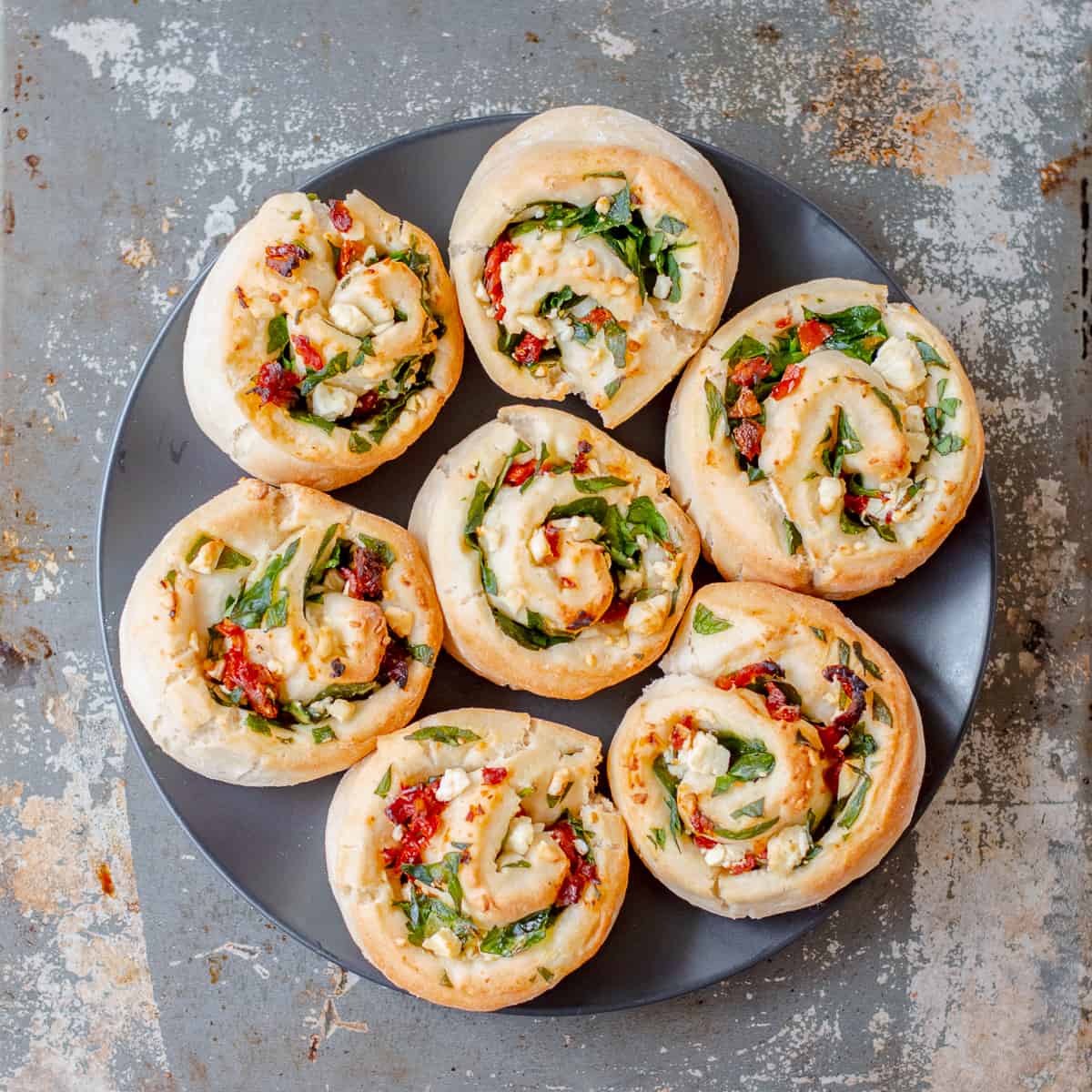 Seven spinach feta sundried tomato scrolls on a dark plate