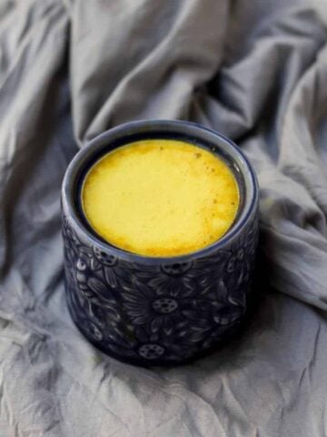 A mug of turmeric latte in blue mug on grey background