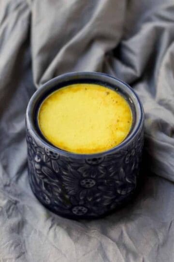 A mug of turmeric latte in blue mug on grey background