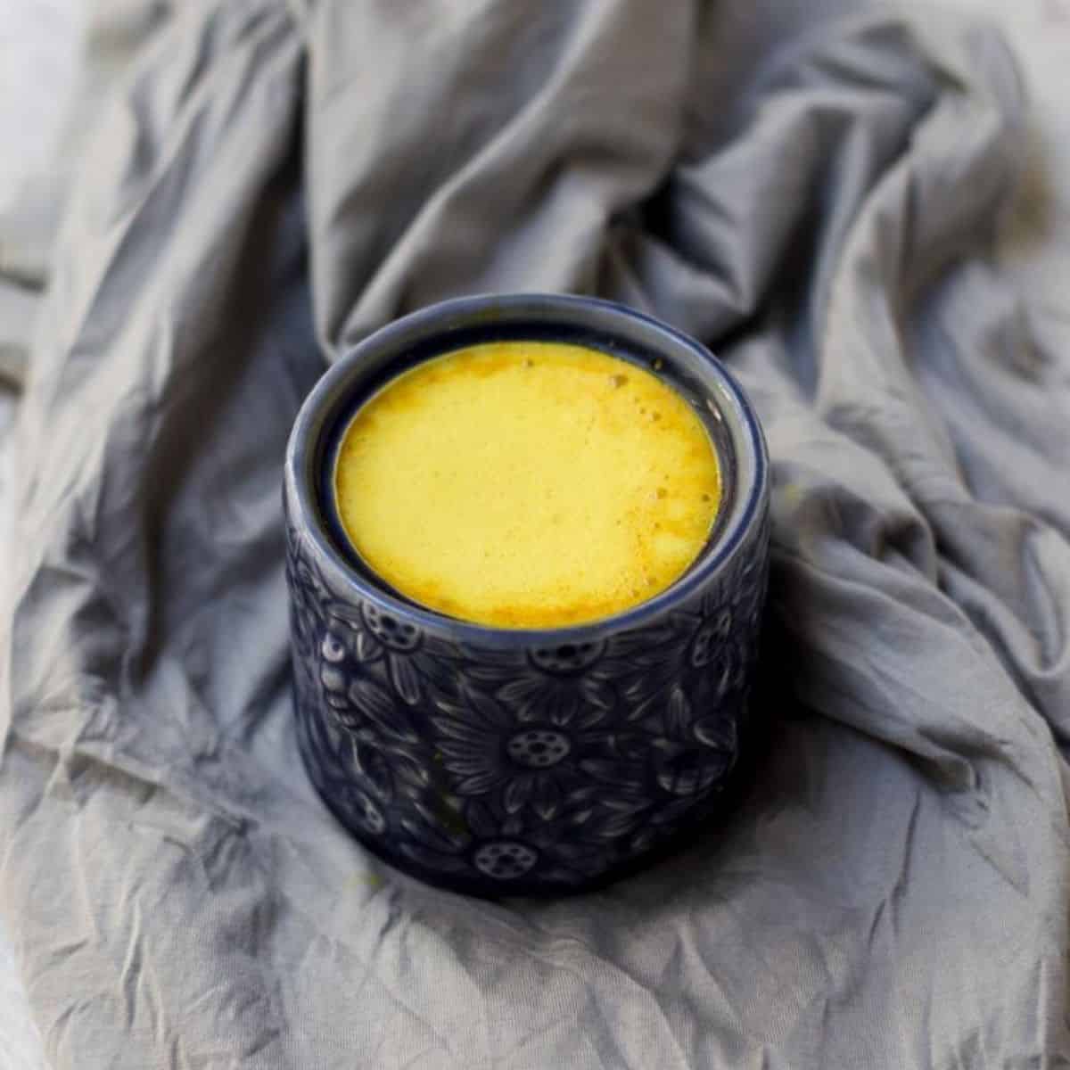 A mug of turmeric latte in blue mug on grey background