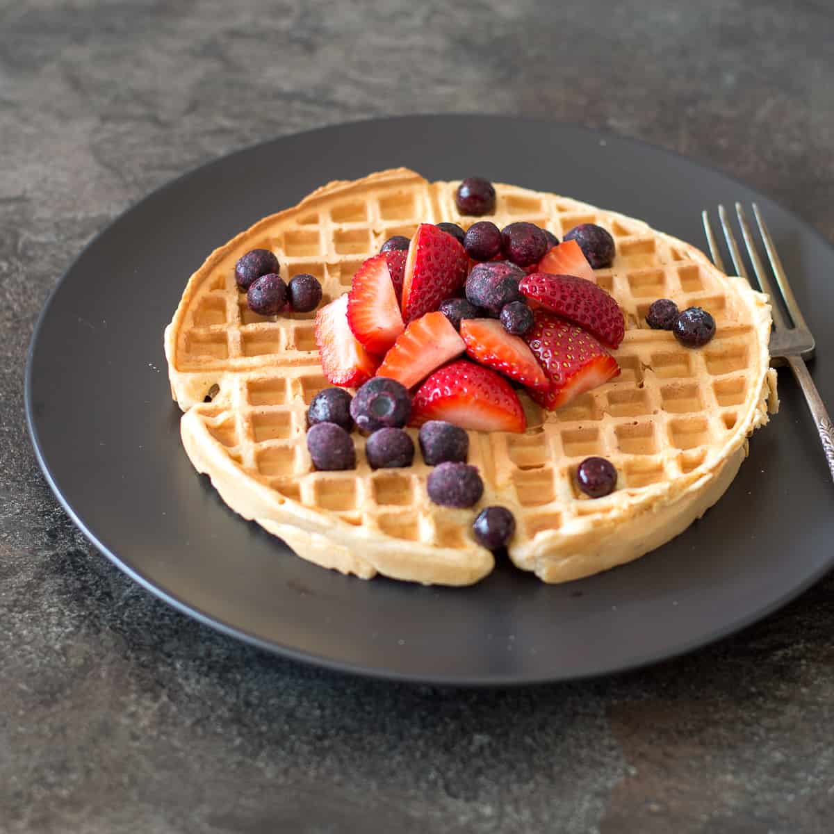 Wholemeal waffles topped with strawberries and blueberries on dark plate