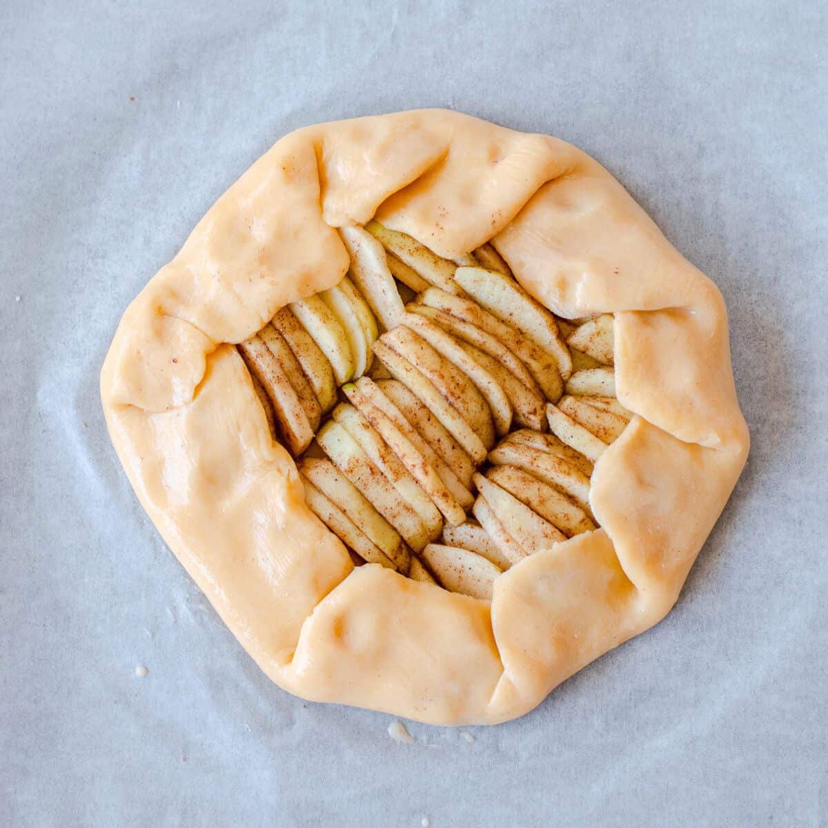 Raw apple galette on a baking tray waiting to be baked.