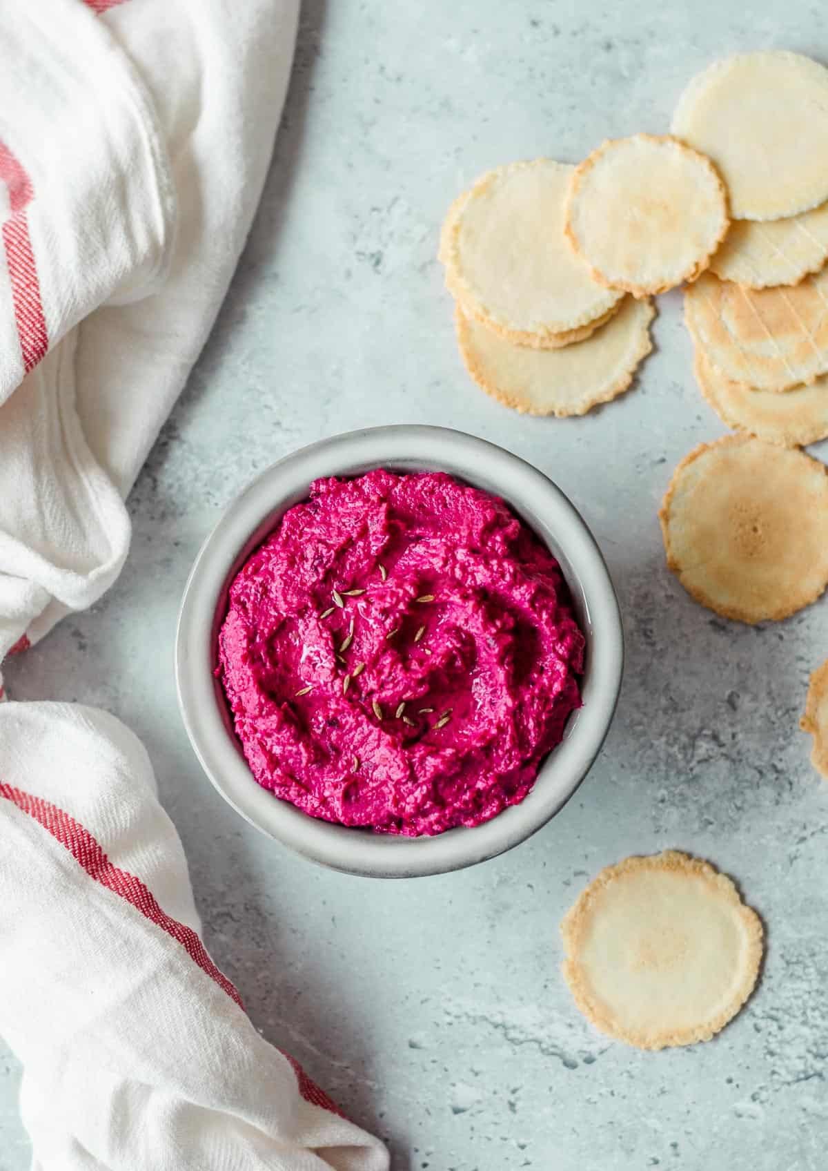 Beetroot hummus in a grey bowl with crackers.