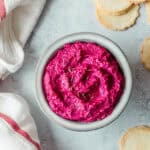 Beetroot hummus in a grey bowl, with crackers and a tea towel.