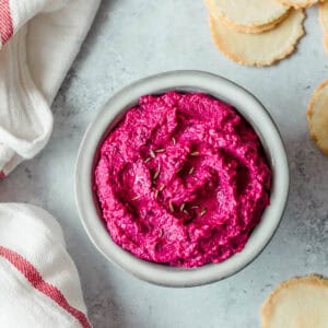 Beetroot hummus in a grey bowl, with crackers and a tea towel.