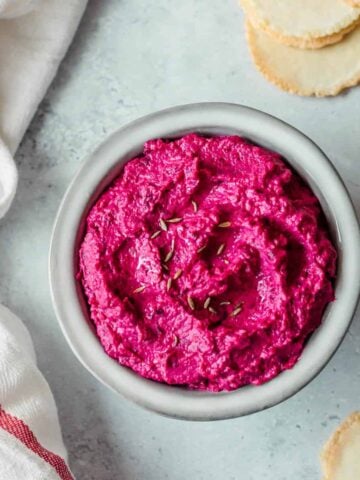 Beetroot hummus in a grey bowl, with crackers and a tea towel.