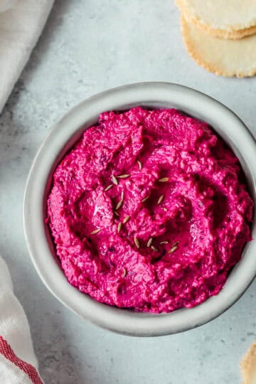 Beetroot hummus in a grey bowl, with crackers and a tea towel.