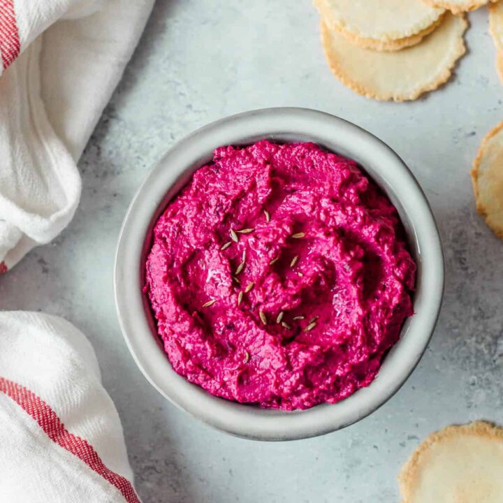 Beetroot hummus in a grey bowl, with crackers and a tea towel.