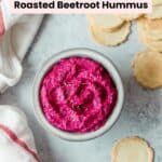 Bright pink beetroot hummus in a grey bowl on a grey background with some crackers.