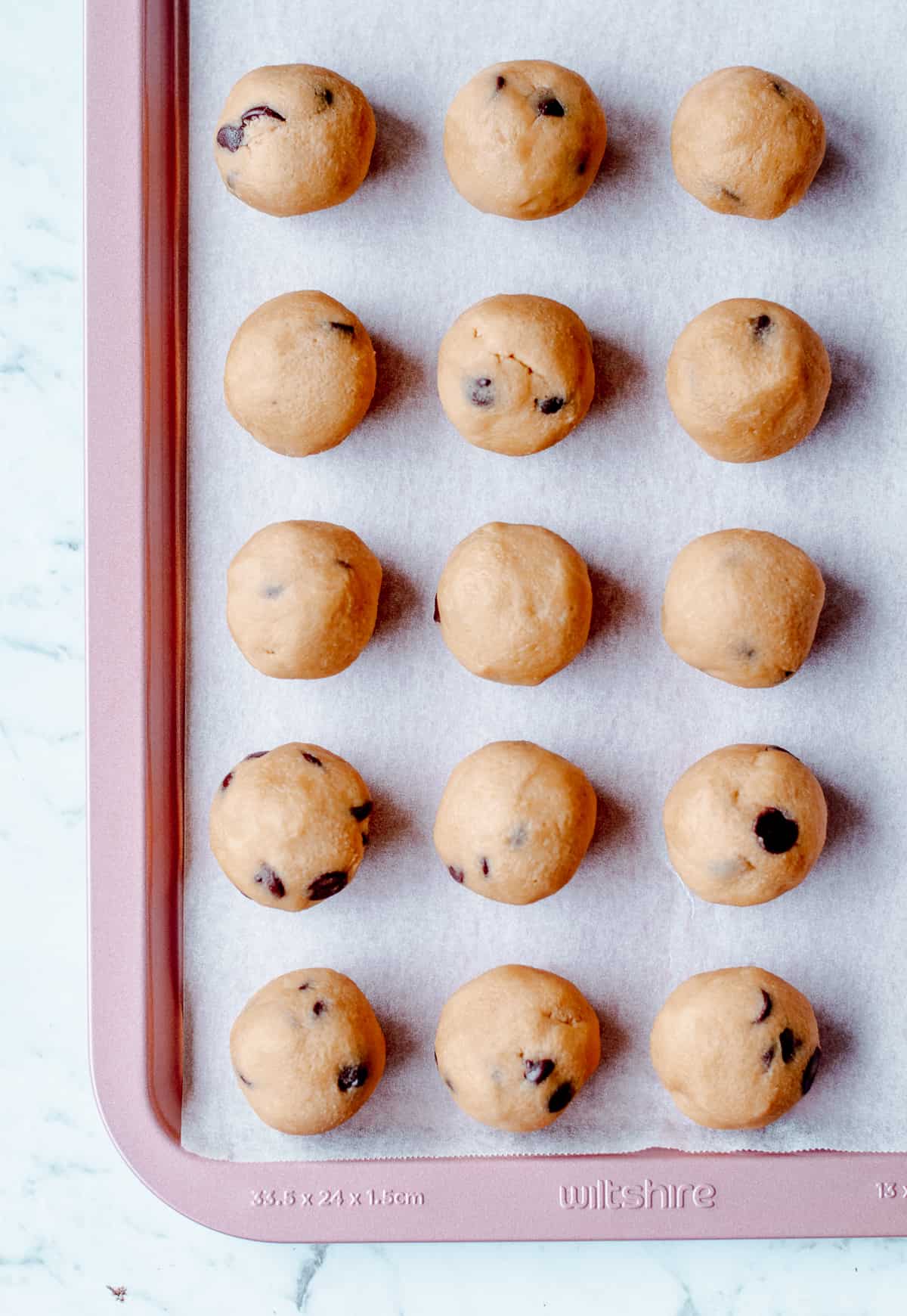 Raw Cookie Dough Balls on pink baking sheet lined with greaseproof paper.