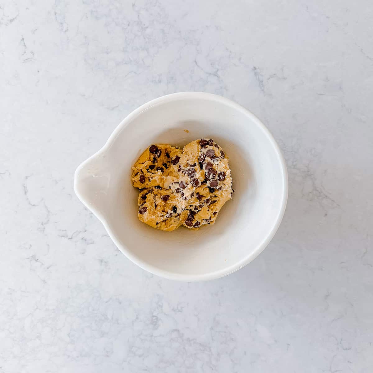 Chocolate chip cookie dough in a cream mixing bowl.