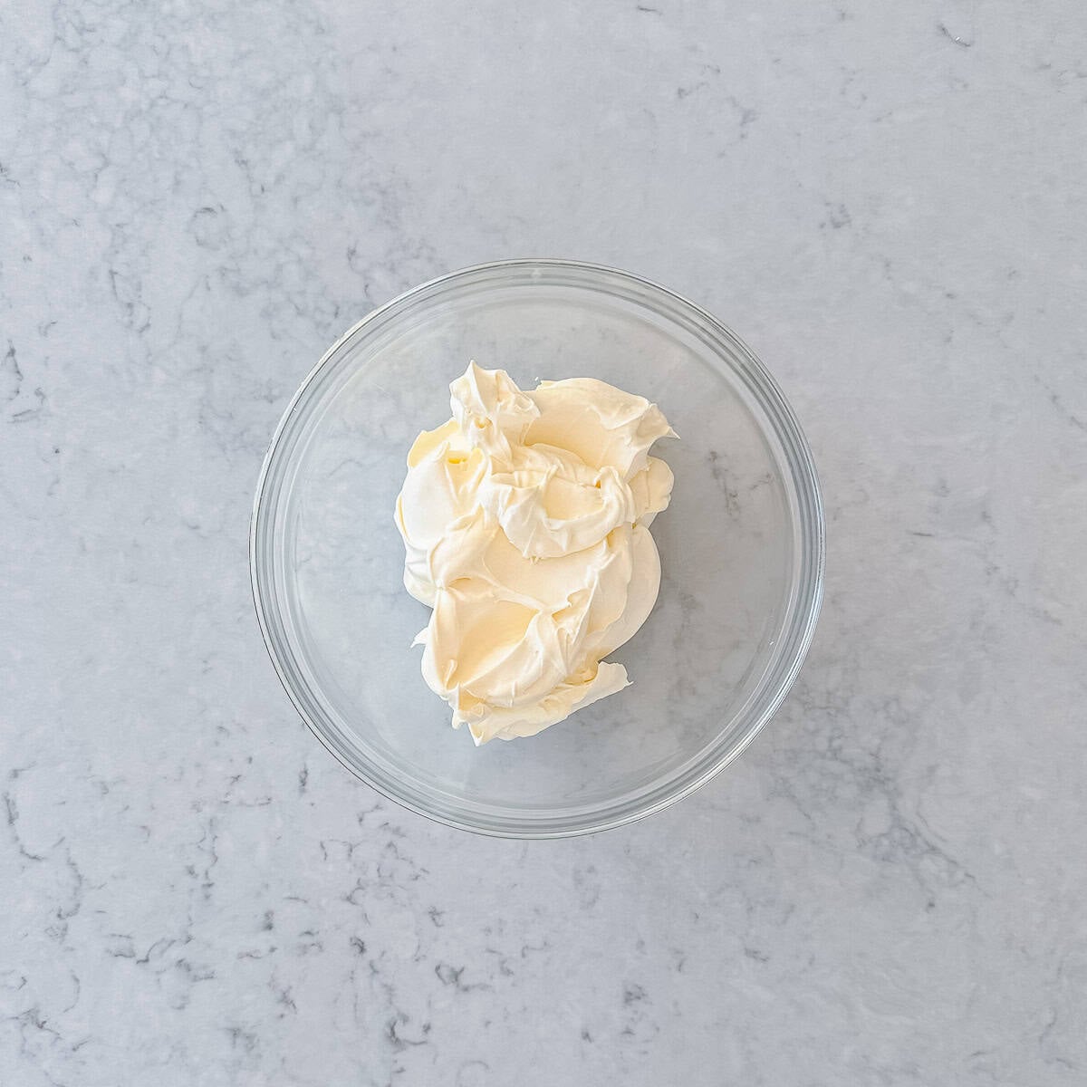 Whipped cream in a glass bowl on a grey marble bench top.