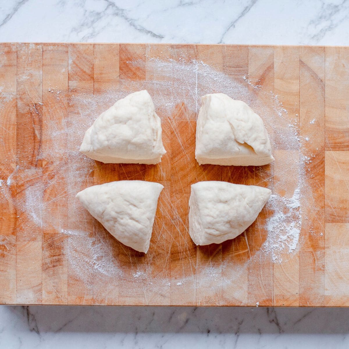 Naan bread dough cut into quarters on a wooden chopping board.