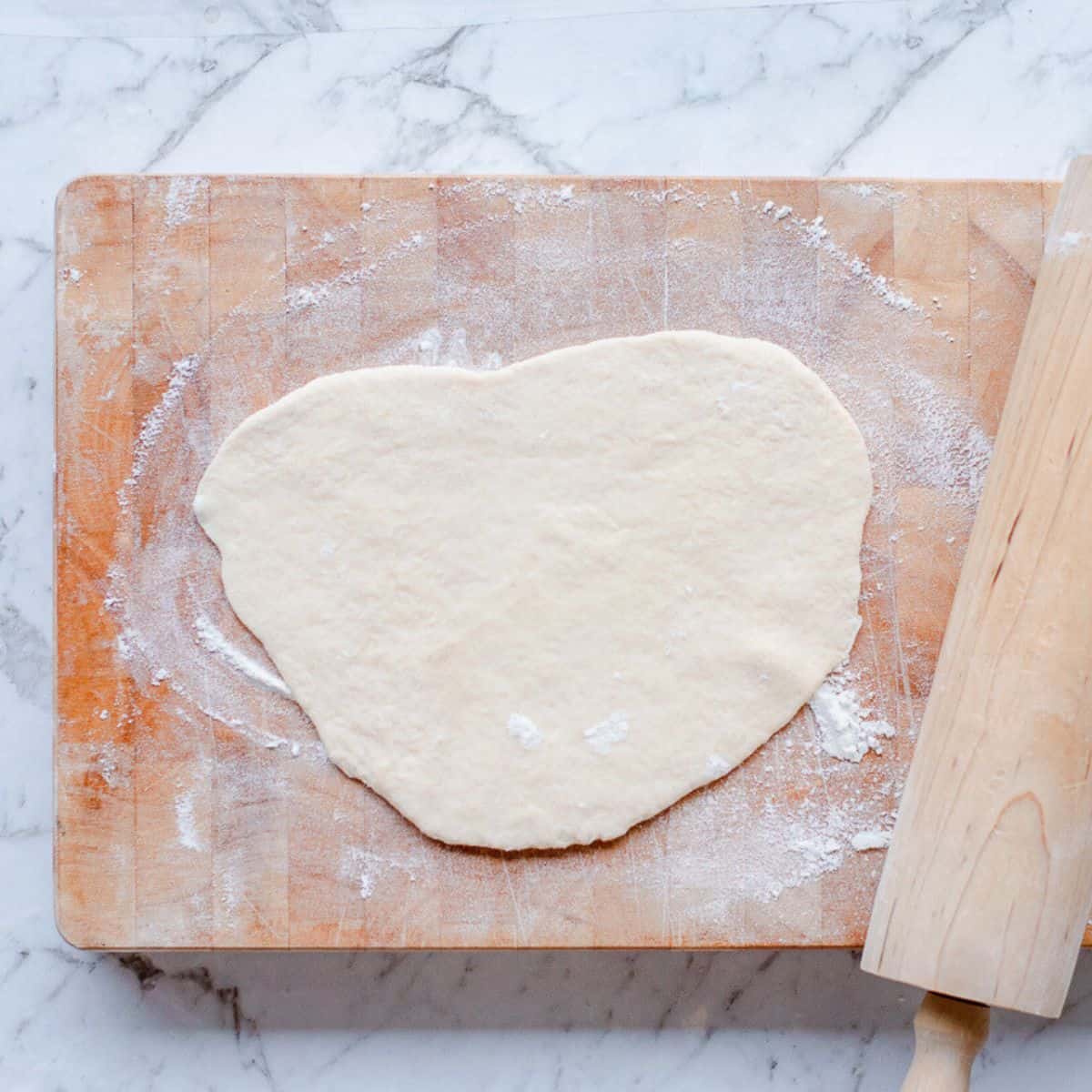 Naan dough rolled out on a wooden chopping board.