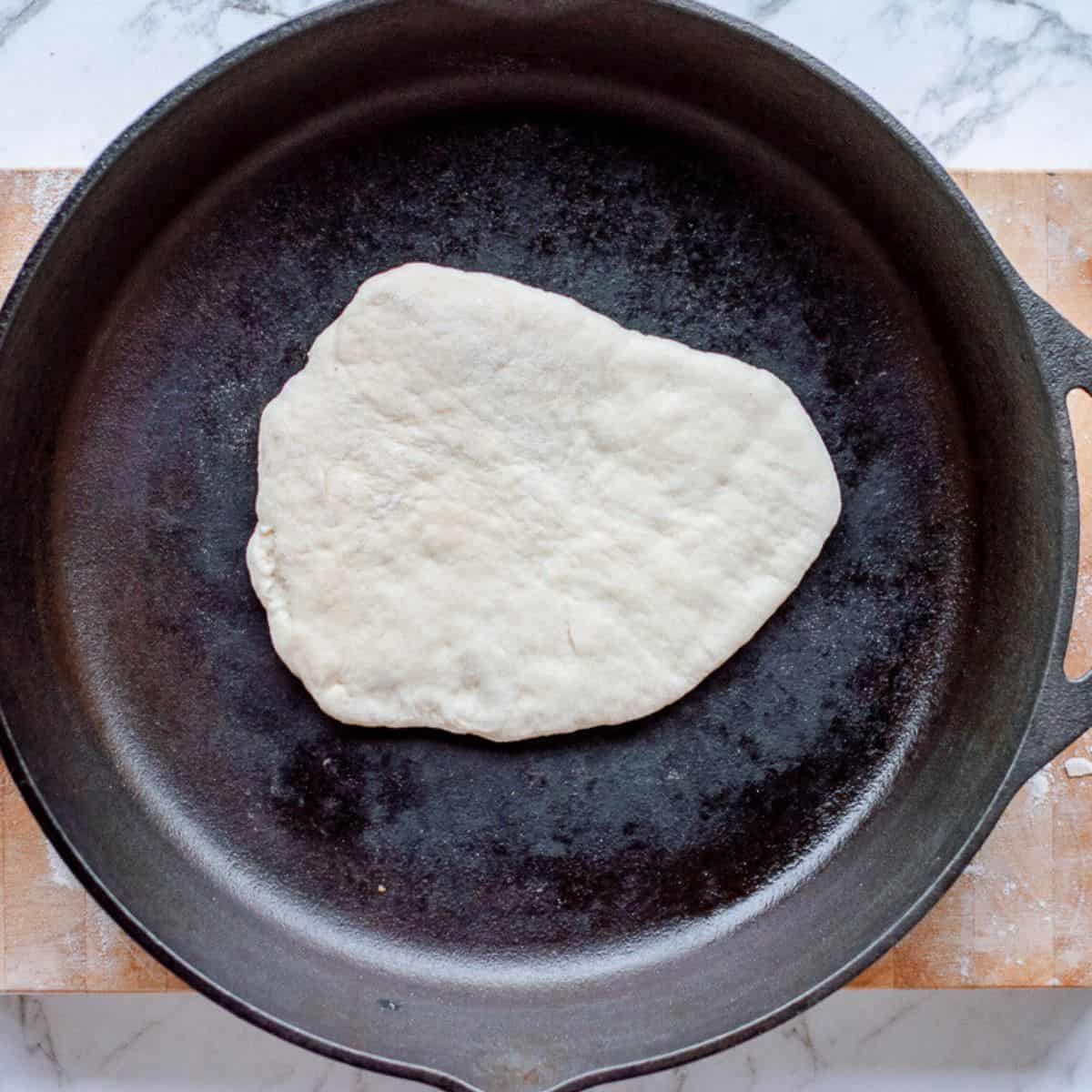 Naan bread being fried in a pan.