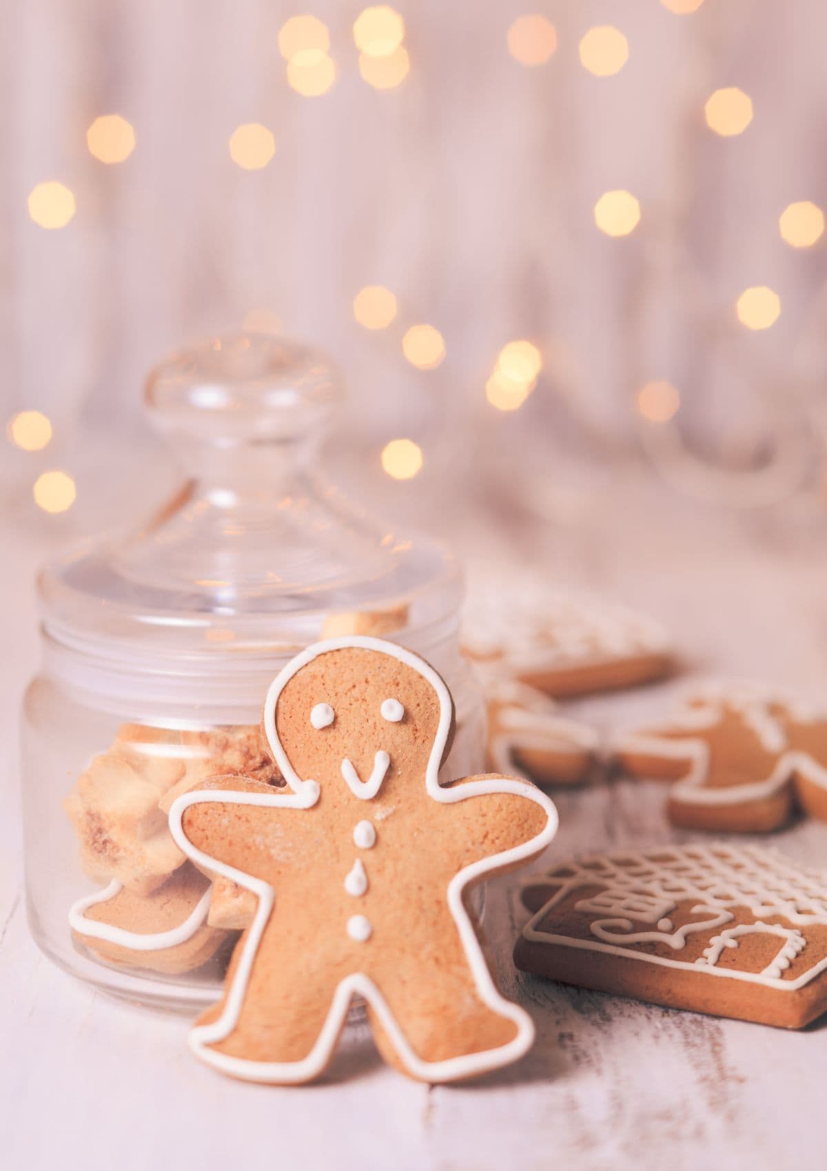 Gingerbread man decorated with white icing resting against a glass jar.