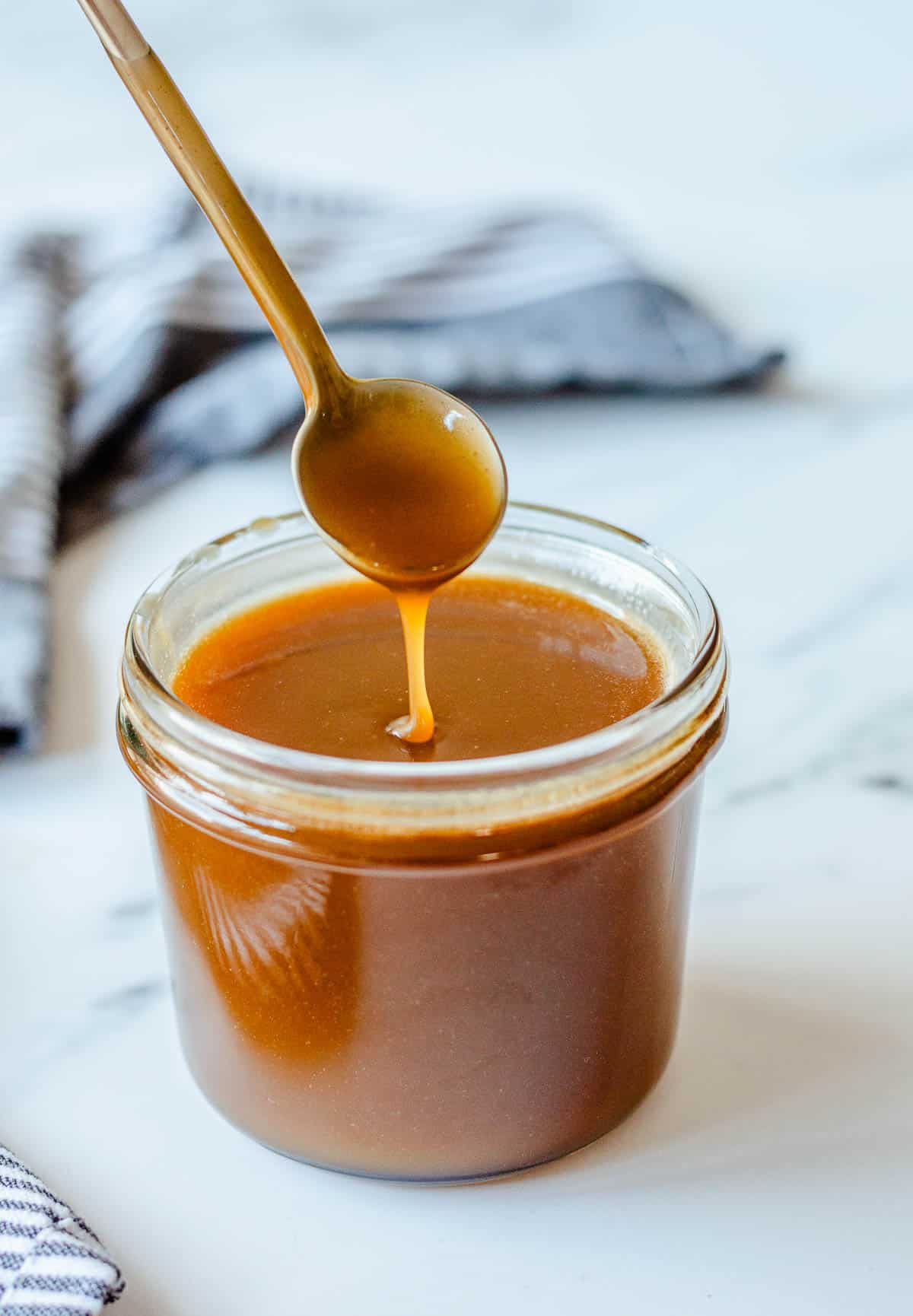 Salted Caramel Sauce in a glass jar with teaspoon.