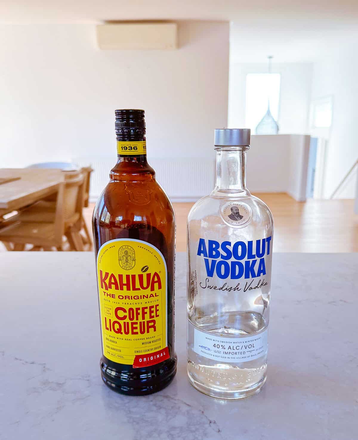A bottle of Kahlúa coffee liqueur and a bottle of Absolut Vodka are placed side by side on a kitchen worktop in a bright, modern dining area.
