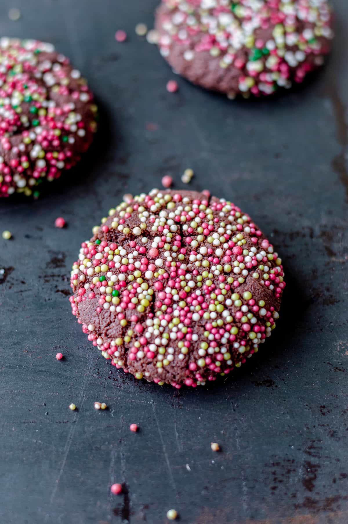 Chocolate cookie covered in sprinkles on dark grey baking tray