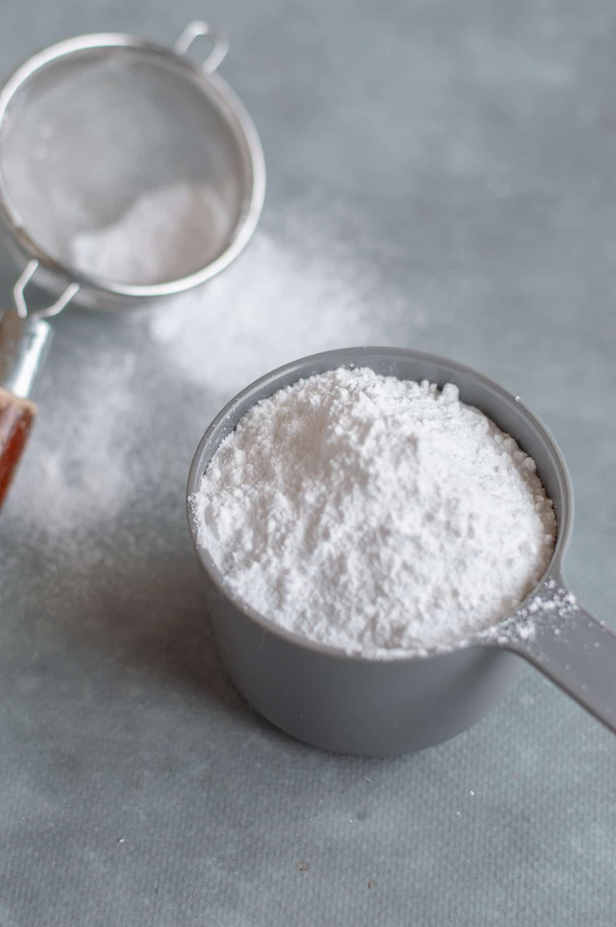 Icing sugar in grey cup with icing sugar sifter