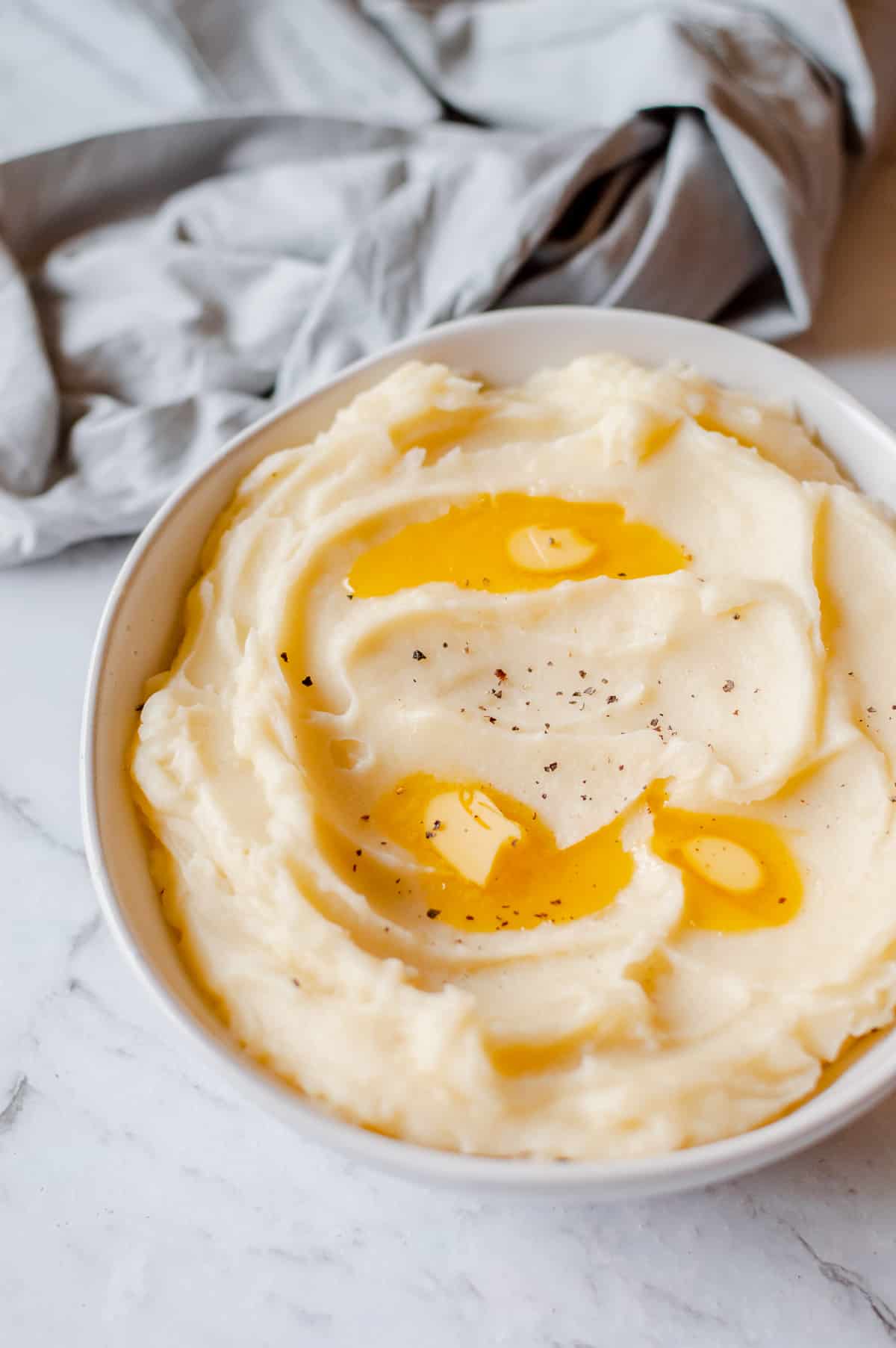 mashed potato in white bowl with melted butter on top.