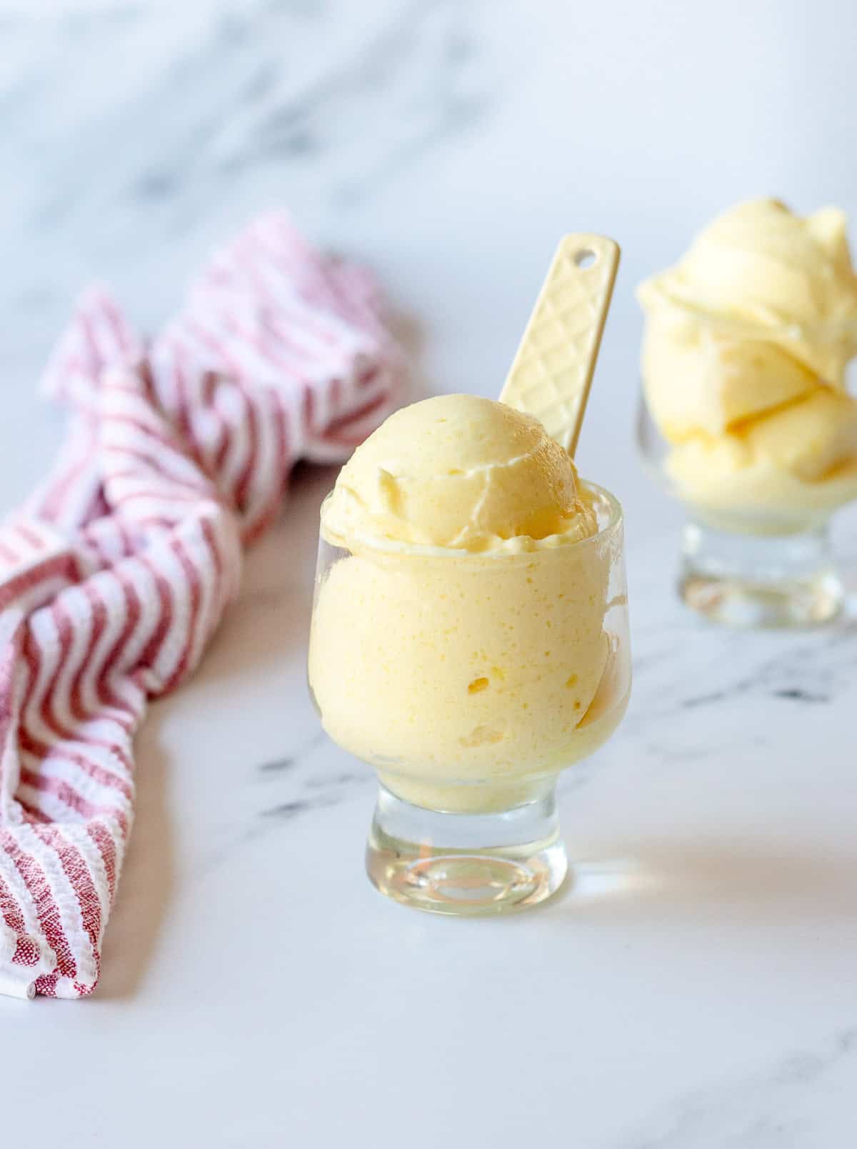 Pineapple sorbet in a glass with yellow spoon and sitting next to a stripy tea towel.