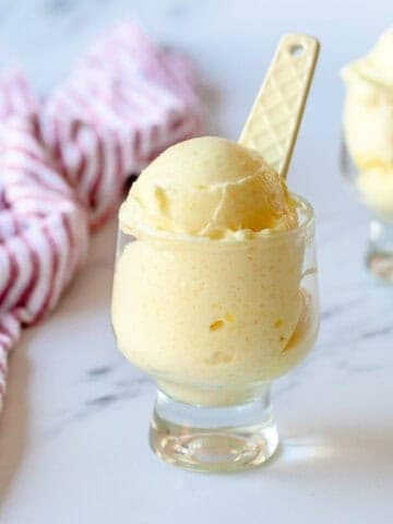 Pineapple sorbet in a clear glass sitting next to a red stripy tea towel.