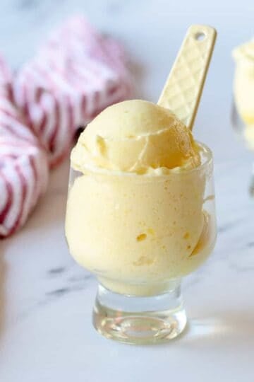 Pineapple sorbet in a clear glass sitting next to a red stripy tea towel.