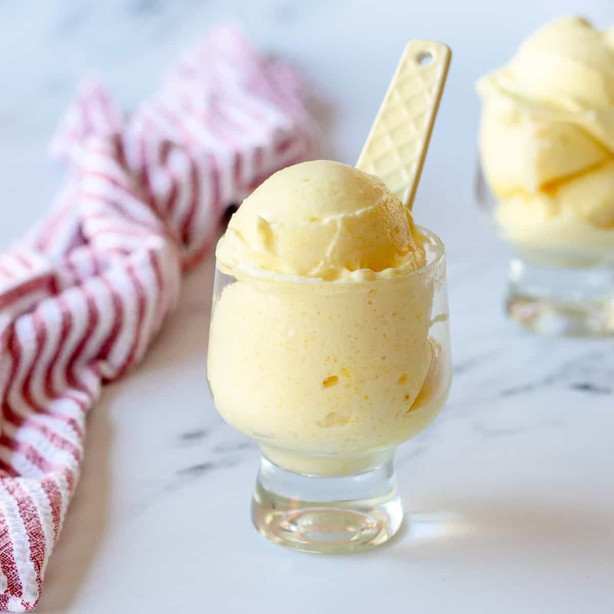 Pineapple sorbet in a clear glass sitting next to a red stripy tea towel.