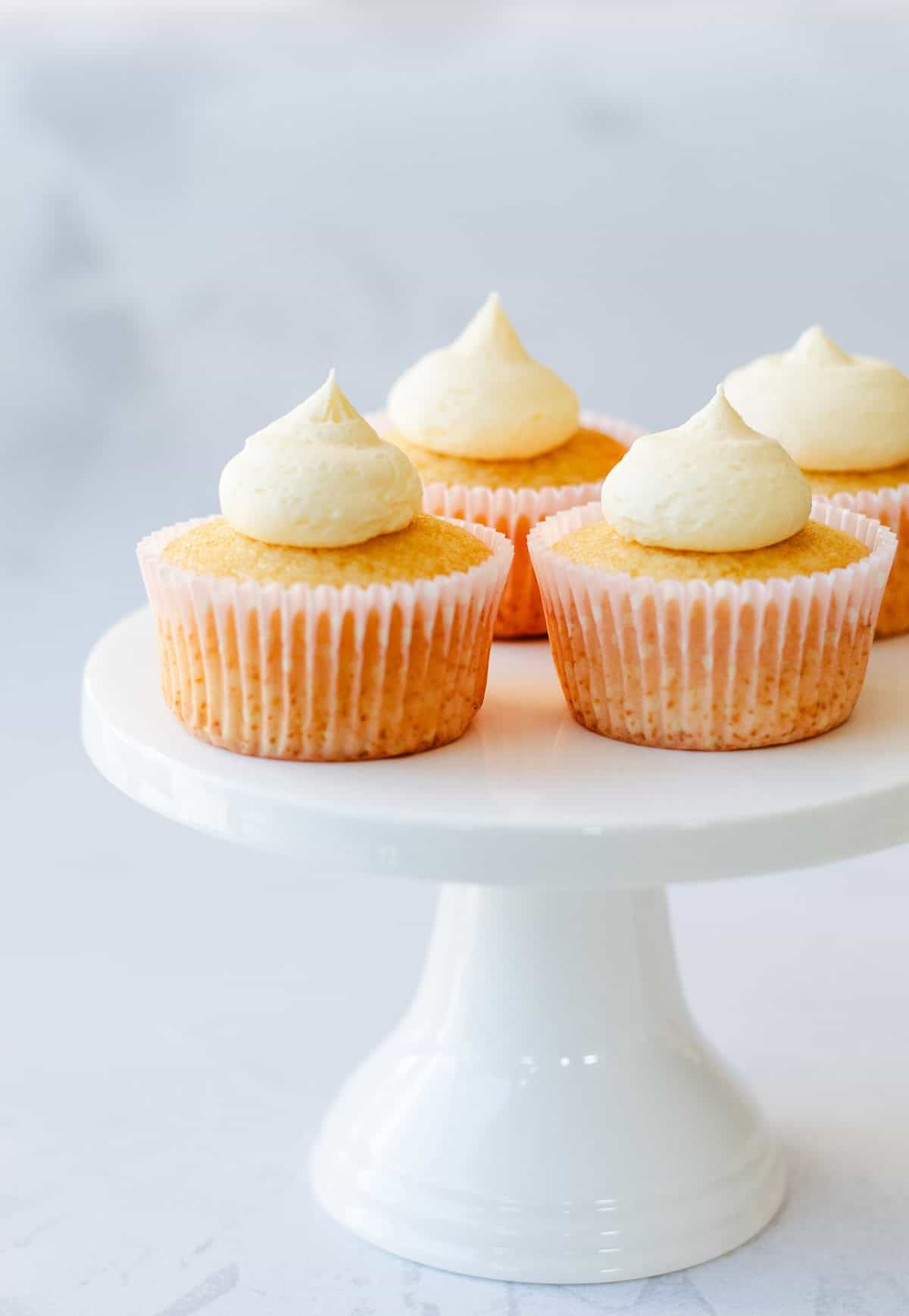Four cupcakes topped with buttercream icing sitting on a white cake stand.